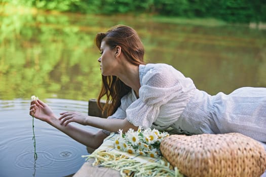 a woman in a light dress lying on a pier by the lake holds a chamomile flower in the water. High quality photo