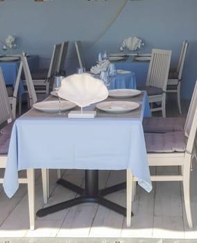Beautiful table setting with glasses, tablecloth, plates in a nautical style in a fish restaurant, blue tinted.