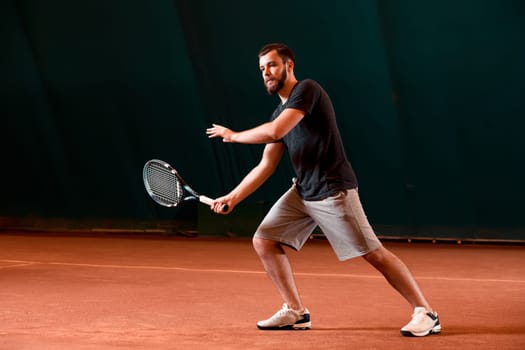 Handsome young man in t-shirt holding tennis racket and looking concentrated while standing on tennis court