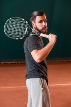 Handsome young man in t-shirt with racket on indoor tennis court