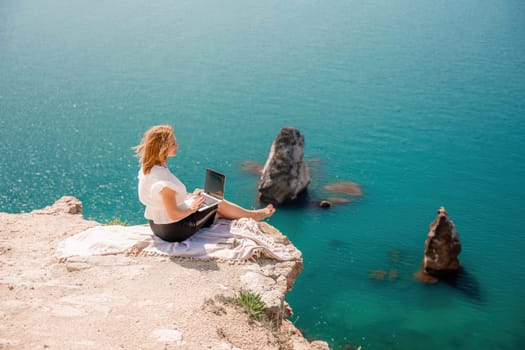 Freelance woman working on a laptop by the sea, typing away on the keyboard while enjoying the beautiful view, highlighting the idea of remote work