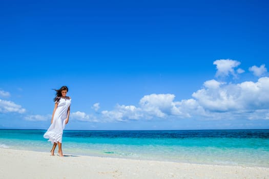 Young woman in white dress walking along sand tropical beach