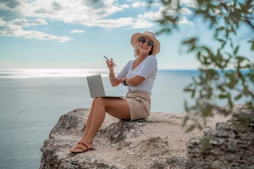 Freelance women sea working on the computer. Good looking middle aged woman typing on a laptop keyboard outdoors with a beautiful sea view. The concept of remote work