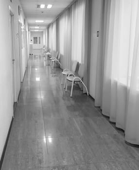 A long corridor with curtains on the windows and chairs in front of the offices, the interior of a modern clinic or office, black and white.