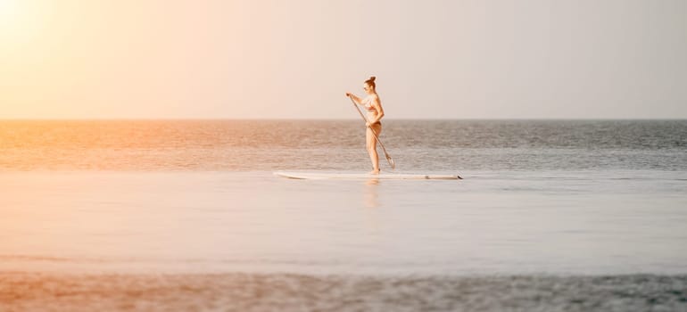 Sea woman sup. Silhouette of happy middle aged woman in rainbow bikini, surfing on SUP board, confident paddling through water surface. Idyllic sunset. Active lifestyle at sea or river