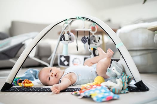 Cute baby boy playing with hanging toys arch on mat at home Baby activity and play center for early infant development. Baby playing at home.