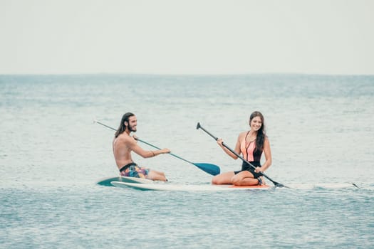 Sea woman and man on sup. Silhouette of happy young woman and man, surfing on SUP board, confident paddling through water surface. Idyllic sunset. Active lifestyle at sea or river