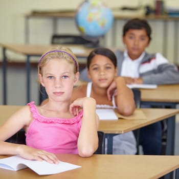 Portrait, serious child and student in classroom with book, ready to learn and study in class. Group of students, education and girl learning in primary school for knowledge, development or studying