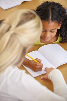 Teacher helping student in classroom, education and writing in notebook with pencil, teaching and learning for development. Scholarship, academic study and young girl and woman in lesson at school.