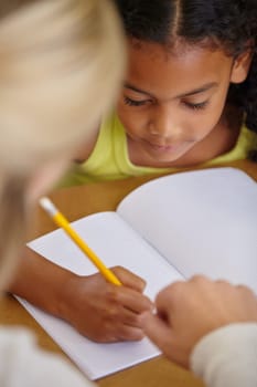 Closeup of teacher helping student, education and writing in notebook, teaching and learning for development. People in classroom to learn, academic study and young girl, woman in lesson at school.