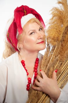 Portrait of heerful funny adult mature woman solokha with sheaf of ears. Female model in national ethnic Slavic style. Stylized Ukrainian, Belarusian or Russian woman in comic photo shoot