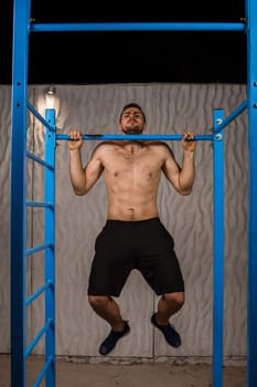 Strong young athlete is engaged in on sports field. Athletic man. Exercises on uneven bars. Athlete Outdoors.