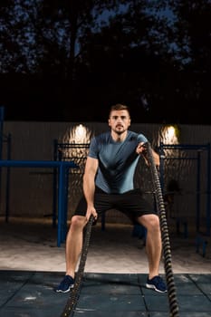 Young man in sportswear training with ropes. Athlete Outdoors