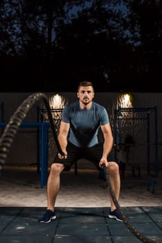 Young man in sportswear training with ropes. Athlete Outdoors