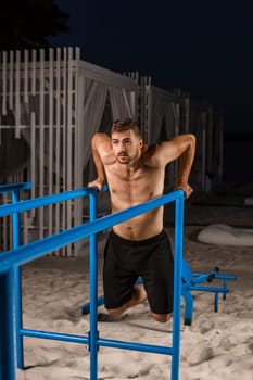 Strong young athlete is engaged in on sports field. Athletic man. Exercises on uneven bars. Athlete Outdoors.
