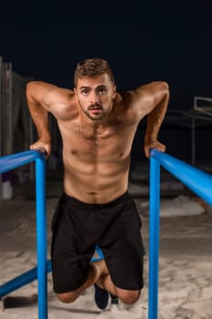 Strong young athlete is engaged in on sports field. Athletic man. Exercises on uneven bars. Athlete Outdoors.
