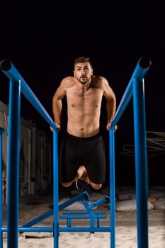 Strong young athlete is engaged in on sports field. Athletic man. Exercises on uneven bars. Athlete Outdoors.