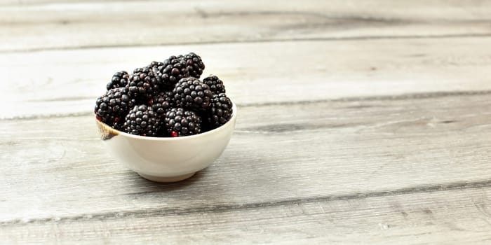 Small bowl with blackberries on wooden desk, space for text on right side.