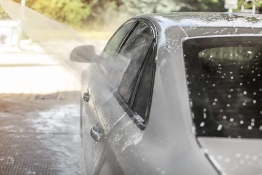 Car washed in self serve carwash, jet stream of water spraying on the side window.