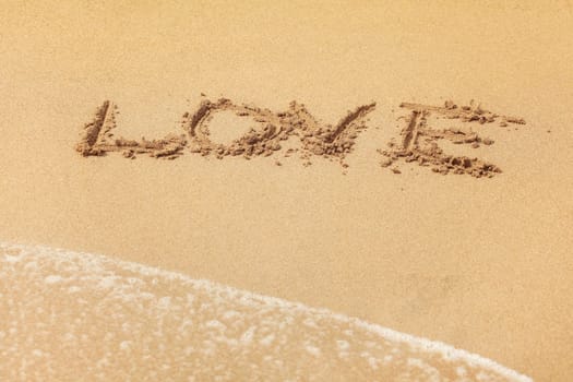 Word LOVE written in wet sand on the beach, sun shining over.