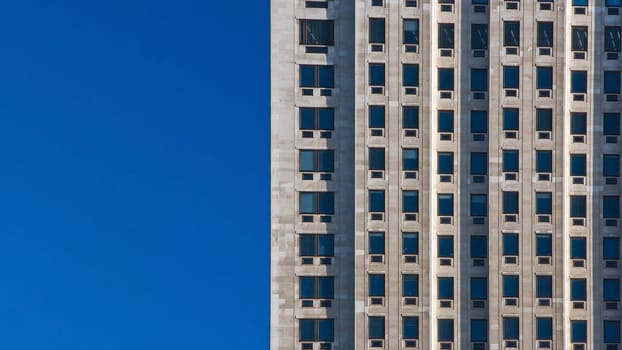 Regular pattern made of rectangular windows on block of flats / offices building. Clear sky (place for text) on left side.