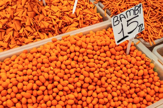Orange (from paprika) spiced nuts and crackers displayed on food market. "Bambi" variety label with price tag in Turkish liras.