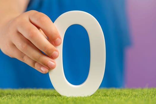 Zero emission concept. A hand holds a white number zero on green grass as a concept of ecology and zero greenhouse gas emissions, preventing climate warming. High quality photo