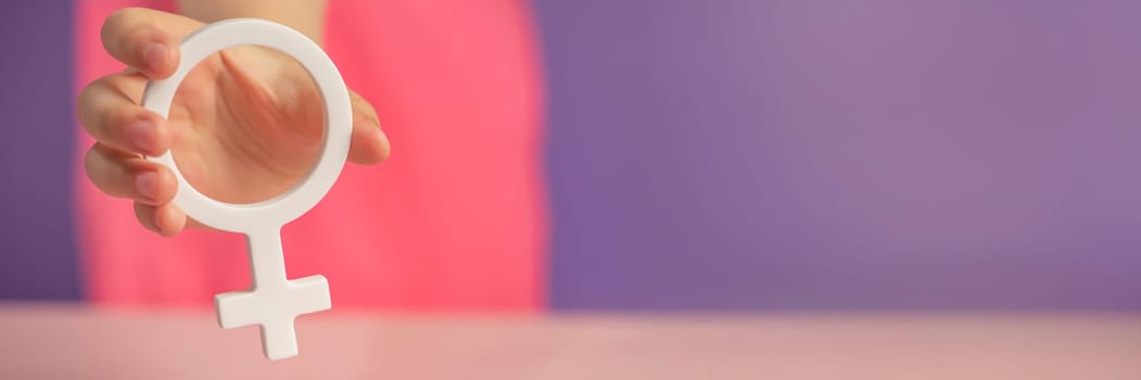 Gender symbol of a woman. Banner with woman symbol in hands on purple background with copy space. The concept of female discrimination, feminism, leadership or domestic violence protest