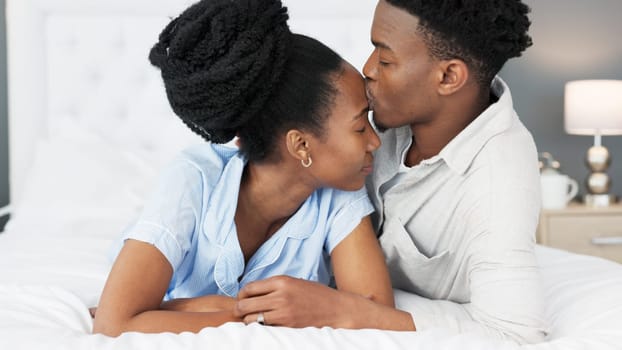 Love, support and trust between black couple sharing a special bond and communication while spending time in the bedroom. Commitment, marriage and understanding with man kissing head of woman.