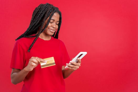 African woman using the mobile and card to shopping online in studio with red background