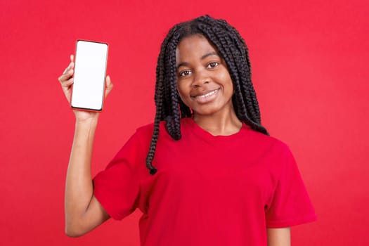 Happy african woman holding a mobile with a blank screen in studio with red background