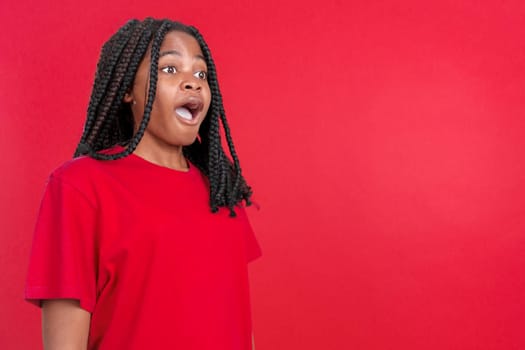 Surprised african woman open the mouth and looking away in studio with red background