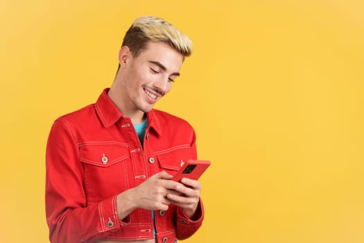 Happy gay man smiling while using the mobile in studio with yellow background