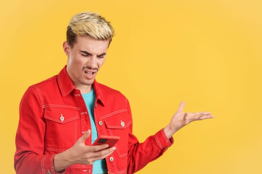 Worried gay man using a mobile phone in studio with yellow background