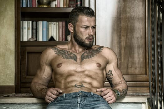 Portrait of sexy shirtless muscular man sitting on stair steps during the day, wearing only jeans