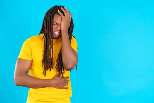 Latin man with dreadlocks gesturing bodily discomfort and headache in studio with blue background