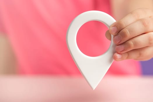 A hand holds a location sign on a purple background. Laying a route, finding the location of a point on the map. Pin icon sign or navigation map locator travel GPS direction pointer