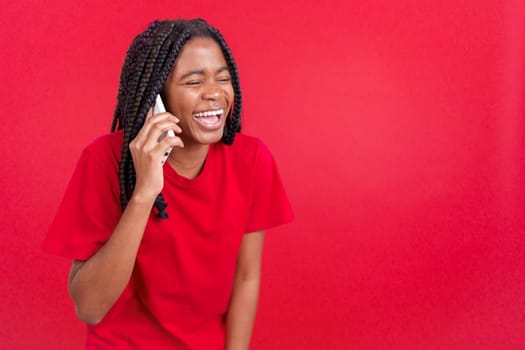 Happy african woman smiling while talking to the mobile in studio with red background