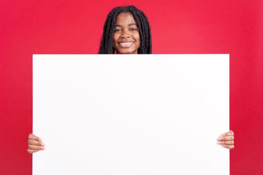 African woman holding a blank panel while smiling at the camera in studio with red background