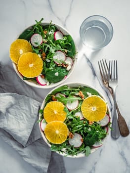 Vegan salad bowl with oranges, spinach, arugula, radish, nut. Top view. Vegan breakfast, vegetarian food, diet concept. Two bowls with salad on white marble tabletop. Vertical