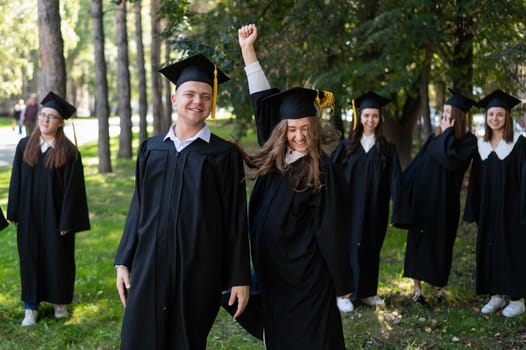 Group of happy young people in graduation gowns outdoors. Students are walking in the park