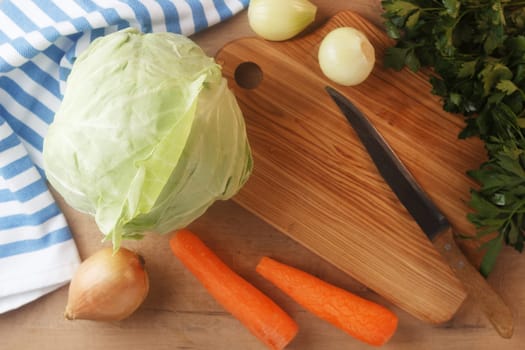 Cabbage lies on a wooden board with carrots, onions and herbs. Preparing to cook cabbage