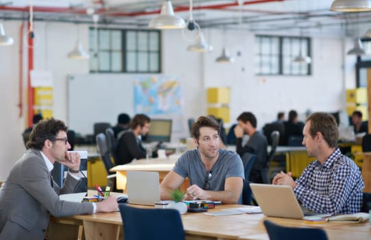 Shot of business colleagues discussing matters with the help of wireless technology in their office.