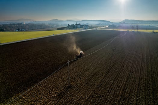 farmer driving a crawler tractor drags a cloud of dust behind, ploughing, power harrowing surface crust breaking to facilitate the birth and seeding of plants on dry soil