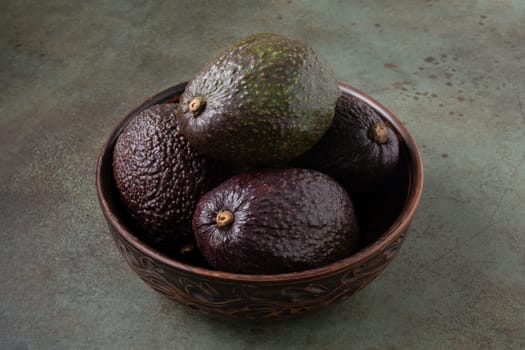 Several ripe avocados lie in a clay bowl. Selective focus.