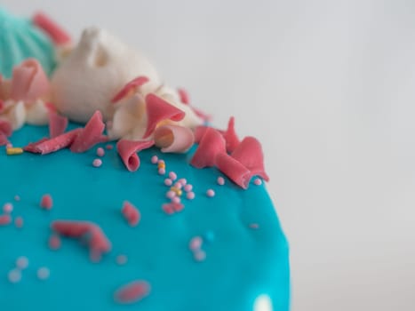 studio shot of chocolate frosted blue dripped icing white cup cake, unicorn , meringue and sprinkles on top