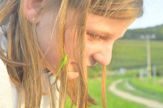A little blonde girl with a grasshopper in her hair. The concept of romance and carefree childhood