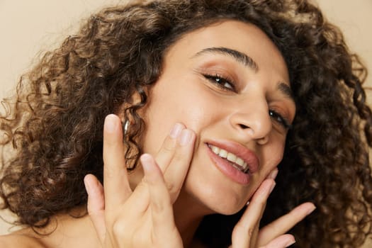 Woman beauty face close-up applying anti-aging moisturizer with fingers of her hand, skin health nails and hair, hair dryer style curly afro hair, body and beauty care concept. High quality photo