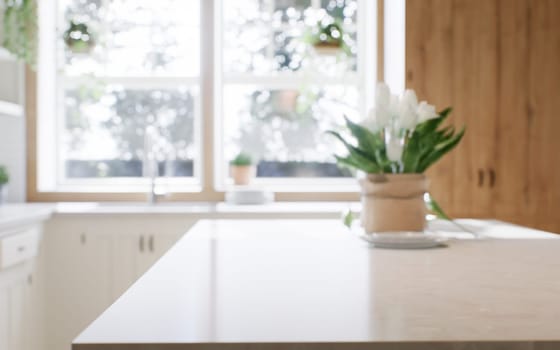 Close-up of a marble countertop of an island kitchen against a blurred background of a kitchen with appliances and utensils by a window with a green plant. 3d rendering