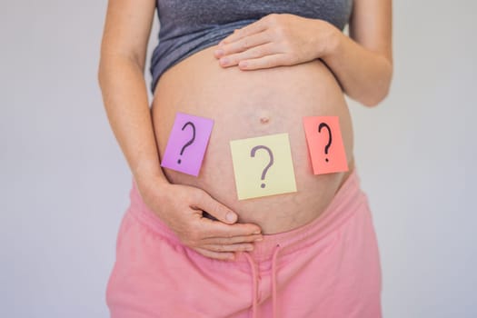 Choosing baby name. Confused pregnant woman with question marks on paper stickers on tummy.